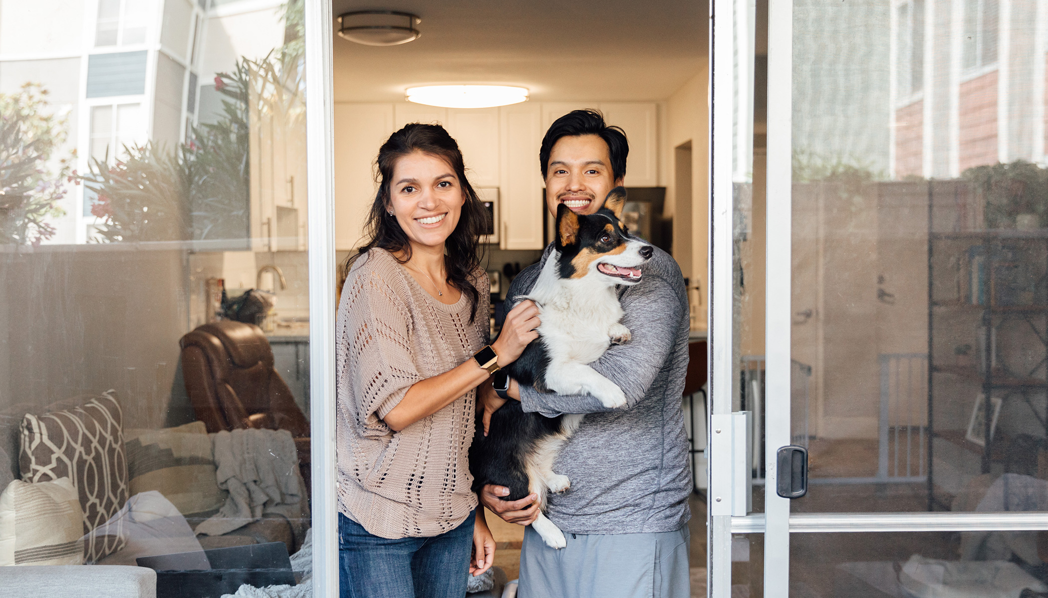 A women smiles and stands close to a man who is holding a Corgi.