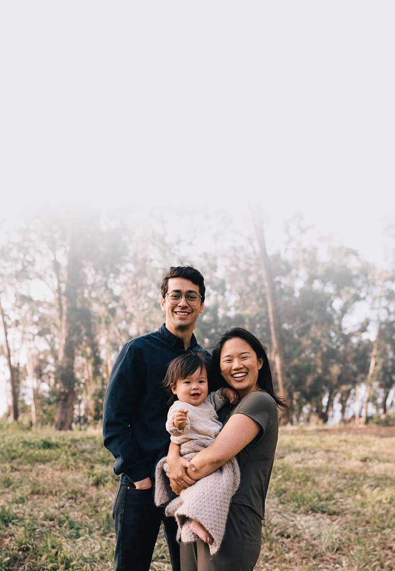 Julio, his spouse and child smile for a picture, surrounded by grass and trees.