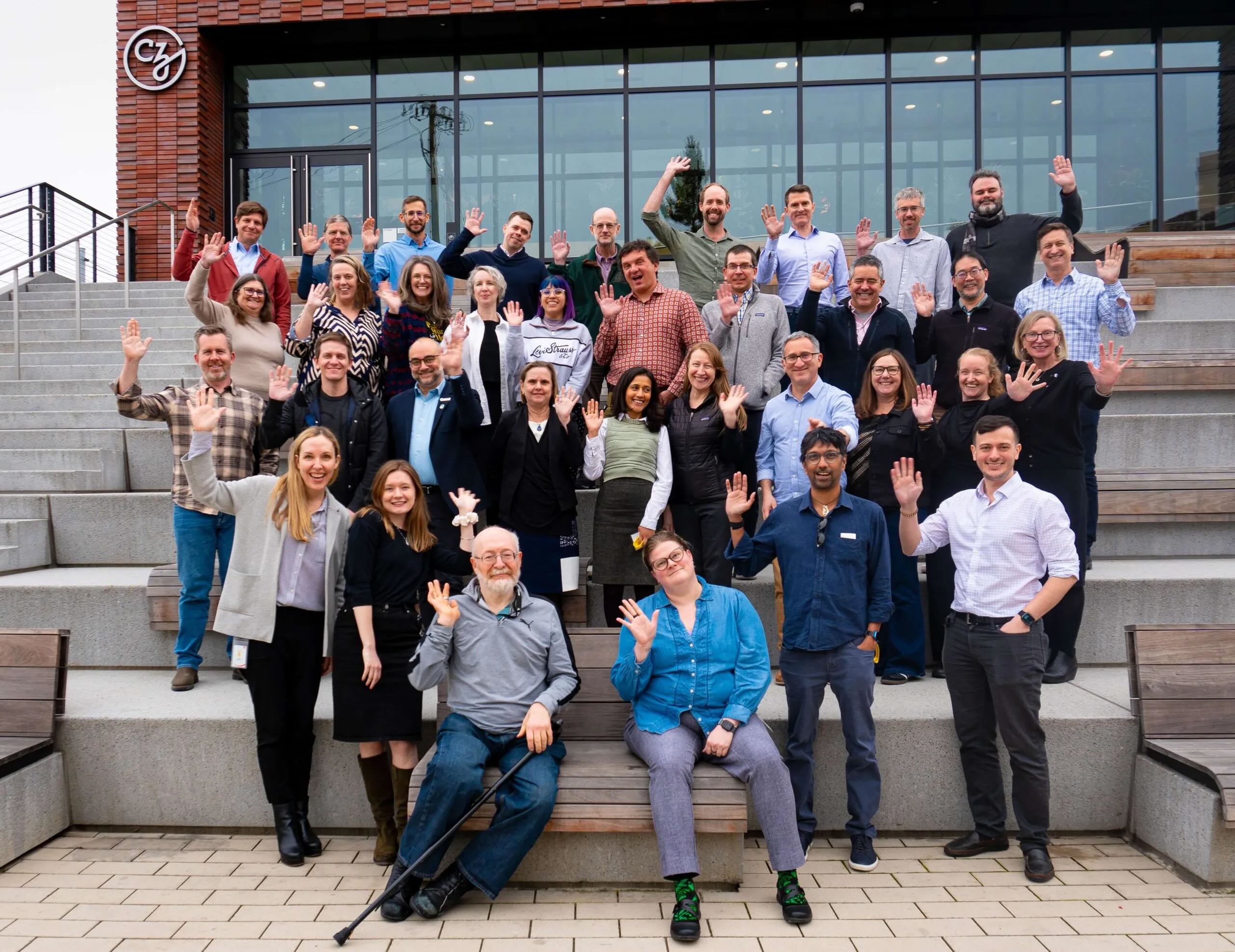 Participants of the CZI Strategic Planning Workshop for Sustaining Scientific Open Source Software stand and wave on the steps of the CZI headquarters in Redwood City, CA.